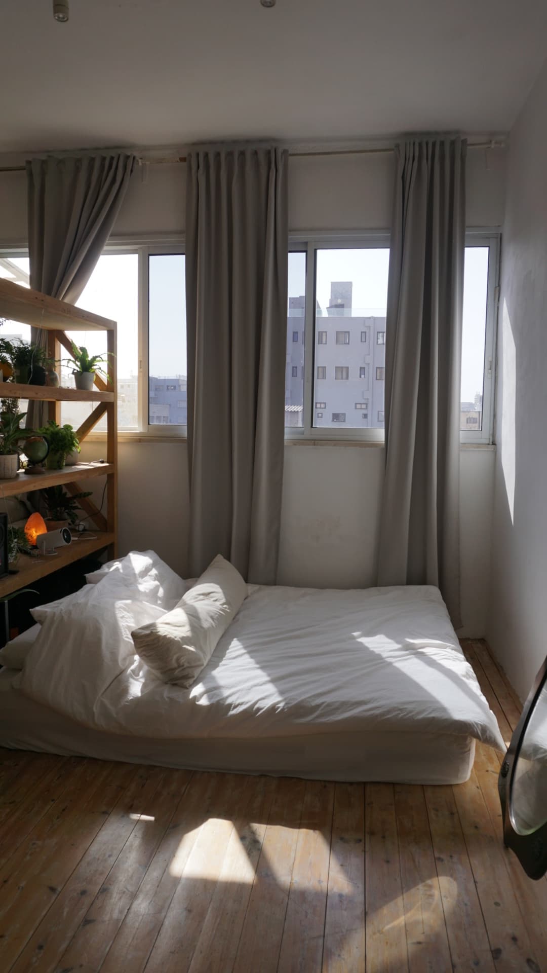 Bedroom corner — low bed, plants, morning sun across the floor